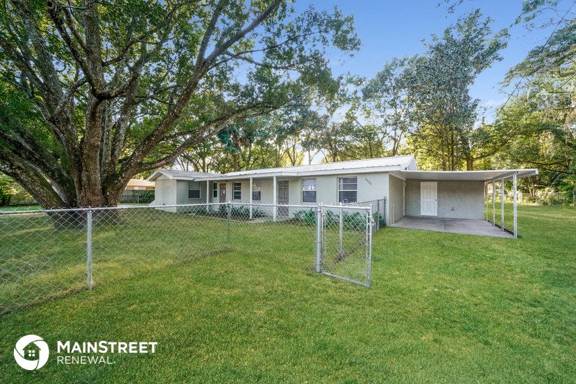 a small white house with a fenced in yard and a tree