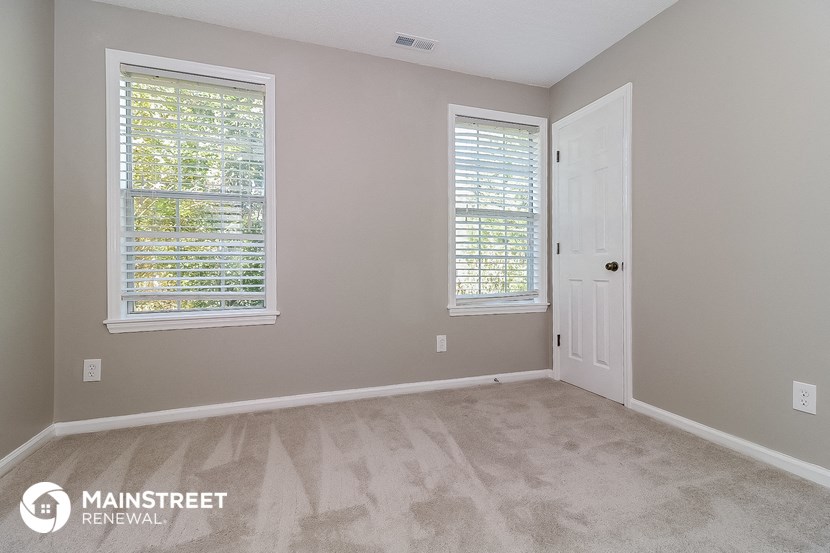 the bedroom of a house with two windows and a door