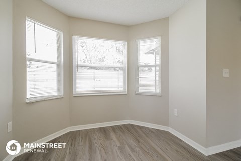 the spacious living room with three windows and wood flooring