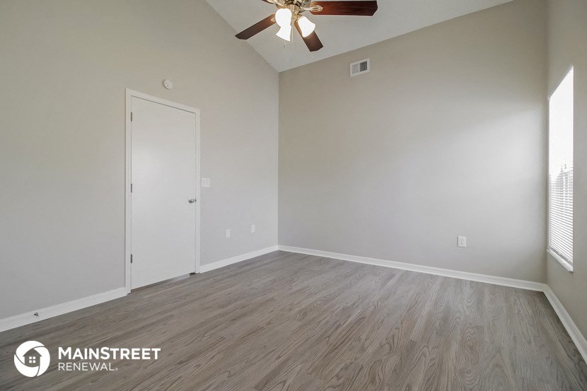 the spacious living room with wood flooring and ceiling fan