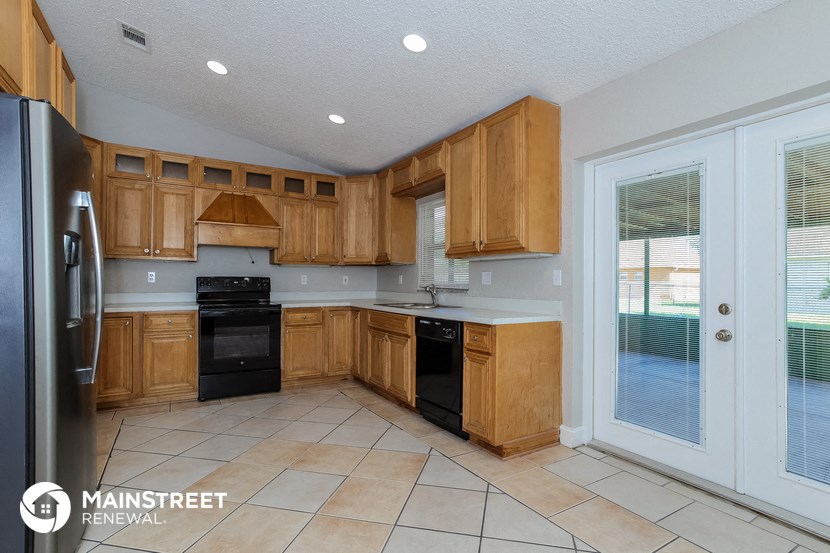 a kitchen with wooden cabinets and black appliances and a door to a patio