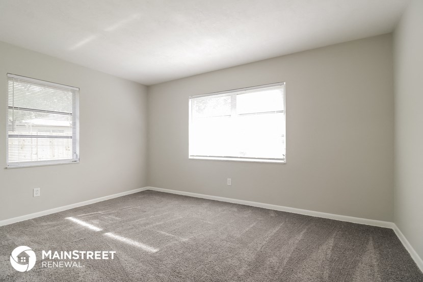 the spacious living room with two windows and carpeting