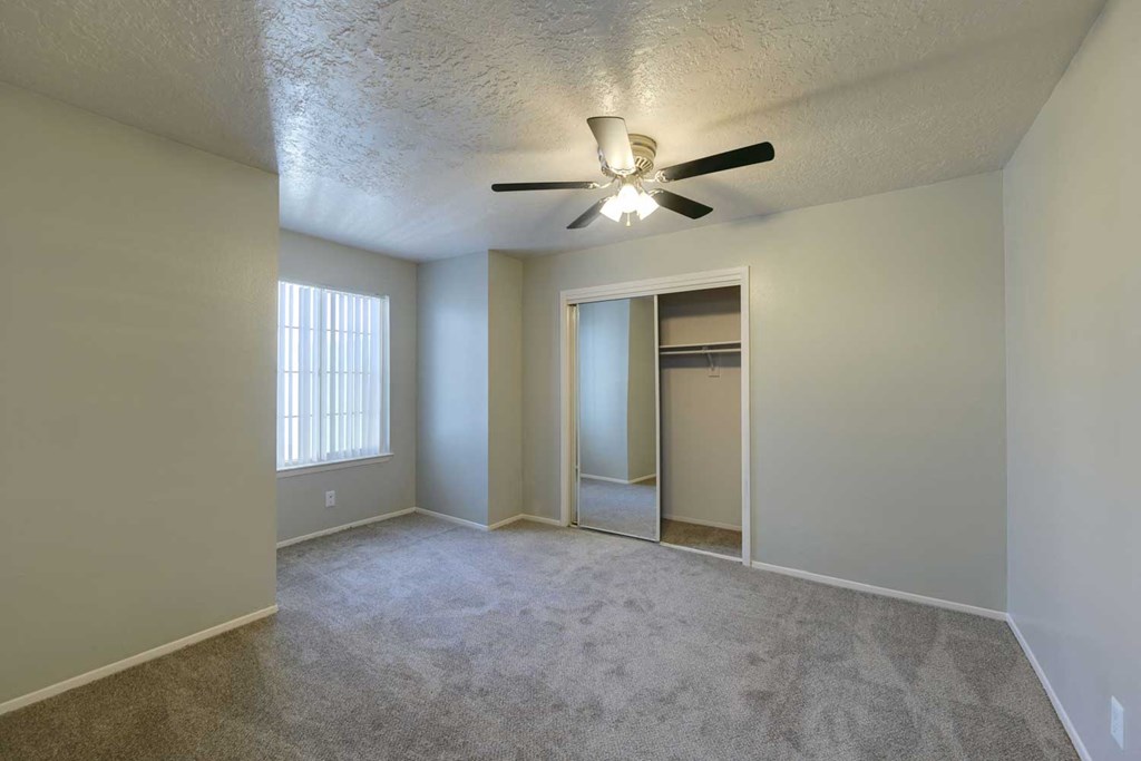 an empty living room with a ceiling fan and a closet