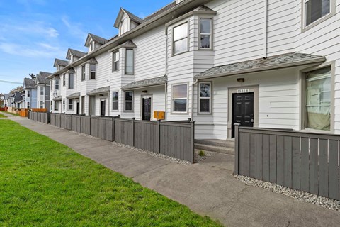 a row of white houses with a sidewalk and grass