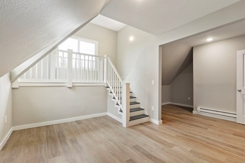 the living room and entryway of a house with white stairs and wood floors