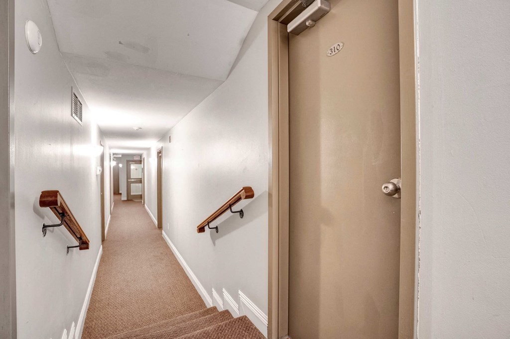a long hallway with a door to a hallway with stairs