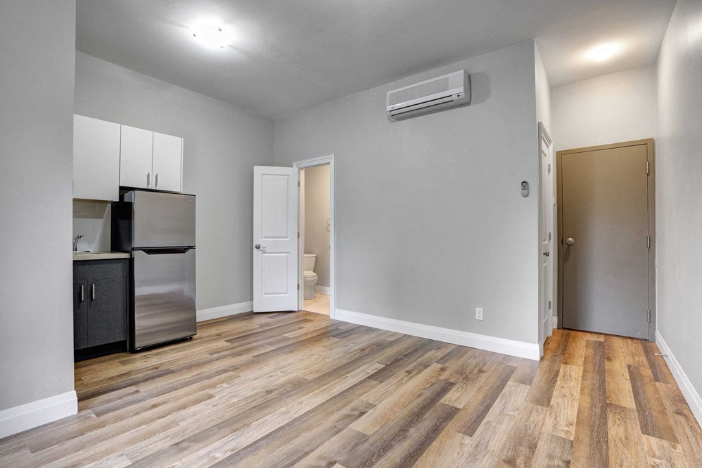 an empty living room with a kitchen and a refrigerator