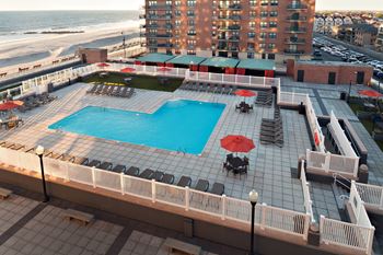 A large pool with a table and chairs is surrounded by a white fence at 10 West Apartments, Long Beach, 11561