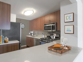 A kitchen with a white counter top and wooden cabinets at 10 West Apartments, Long Beach, NY, 11561