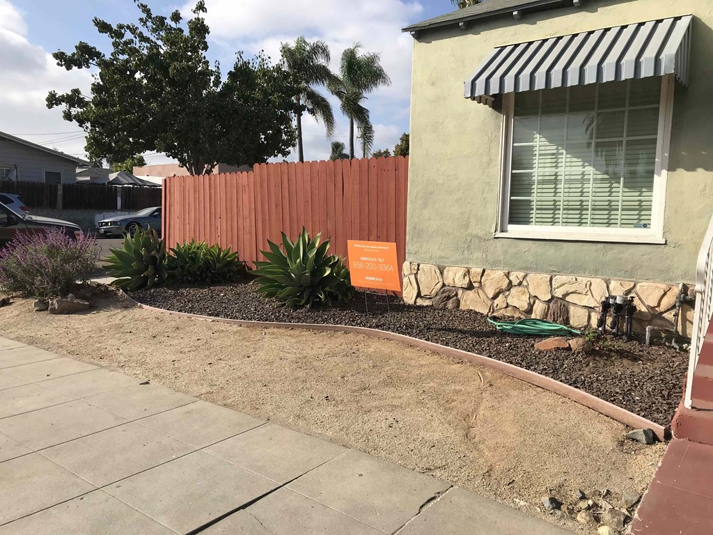 a garden outside a house with a fence and a sign