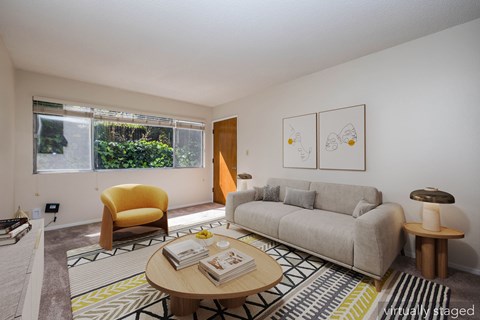 A living room with a yellow chair, a grey couch, a coffee table, and two paintings on the wall.