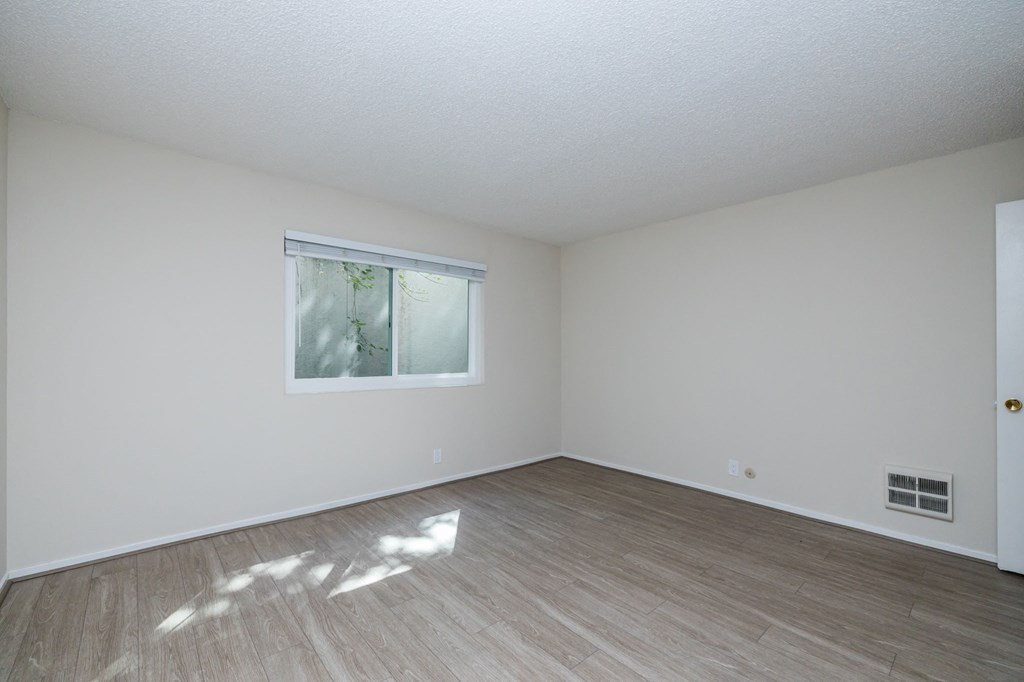 the living room of an empty house with wood flooring and a window