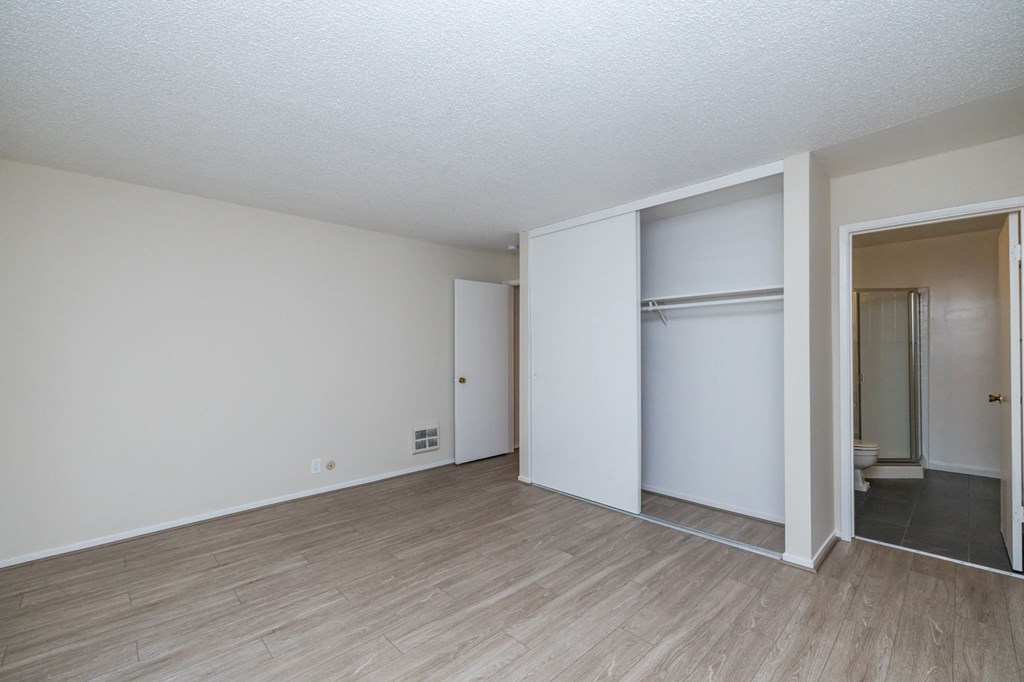an empty living room with white walls and wood flooring and a closet