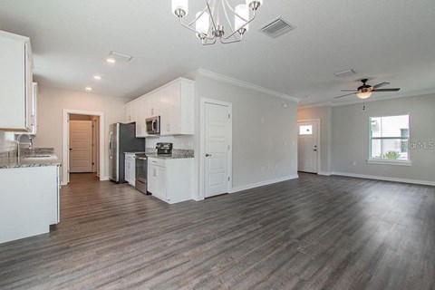 an empty living room with a kitchen and a ceiling fan