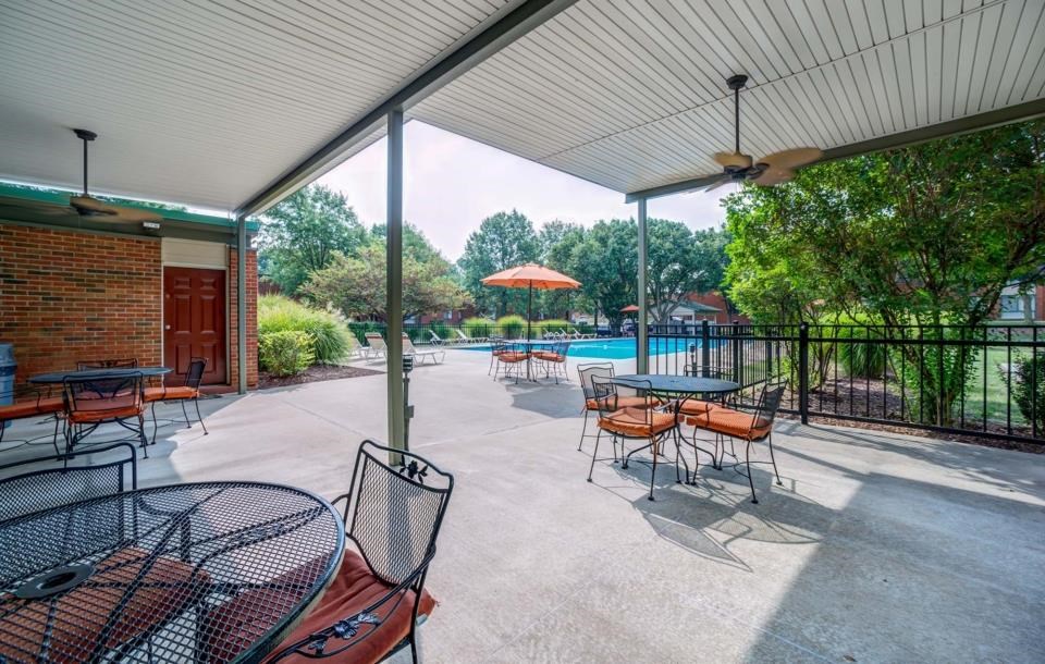 a patio with tables and chairs and a pool in the background