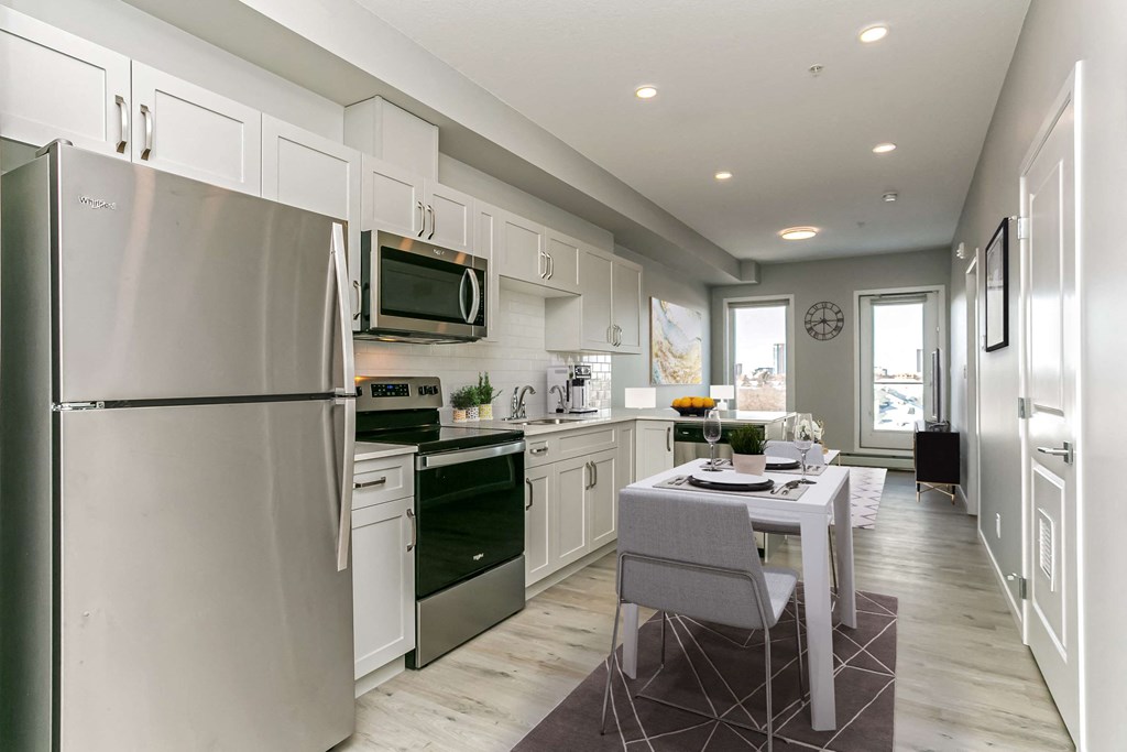 a white kitchen with stainless steel appliances and a dining table