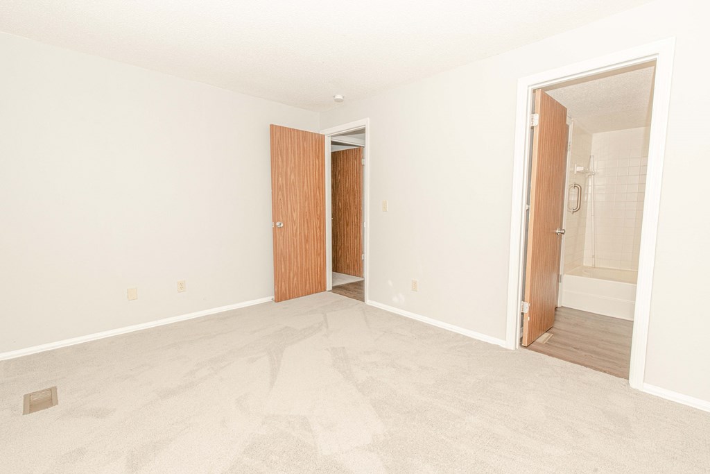 an empty living room with a door to a bathroom and a entrance to a bedroom