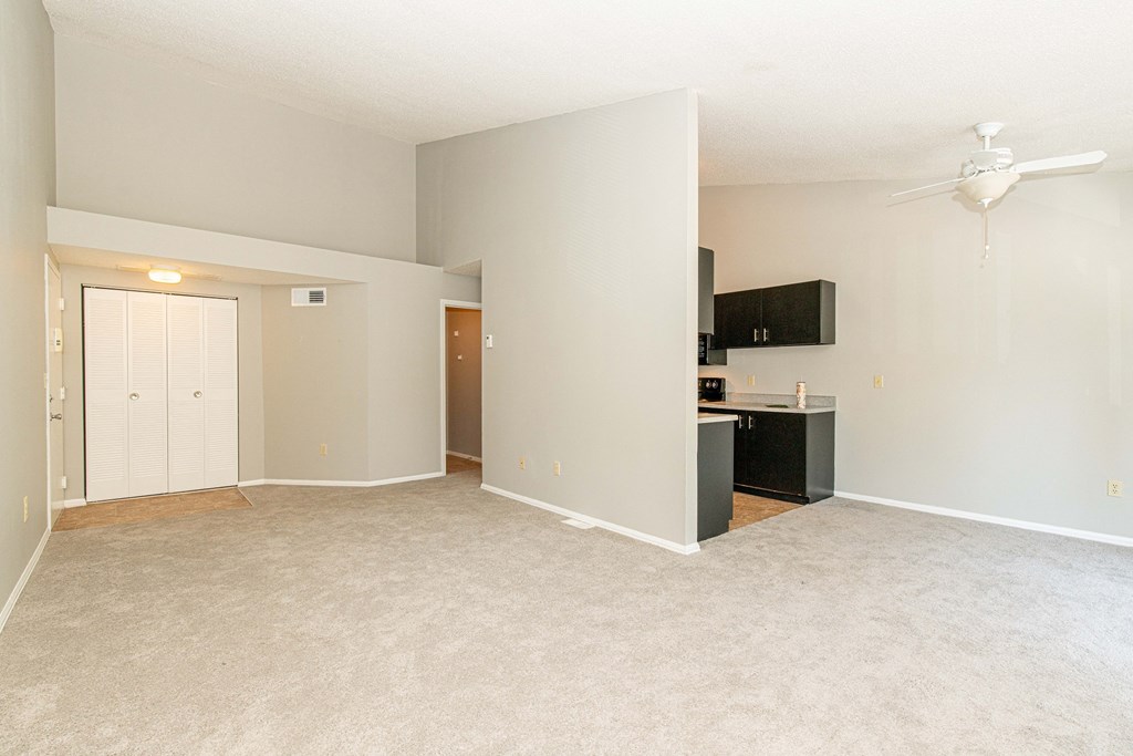 an empty living room with a kitchen and a ceiling fan