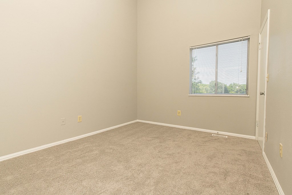an empty bedroom with a window and carpet