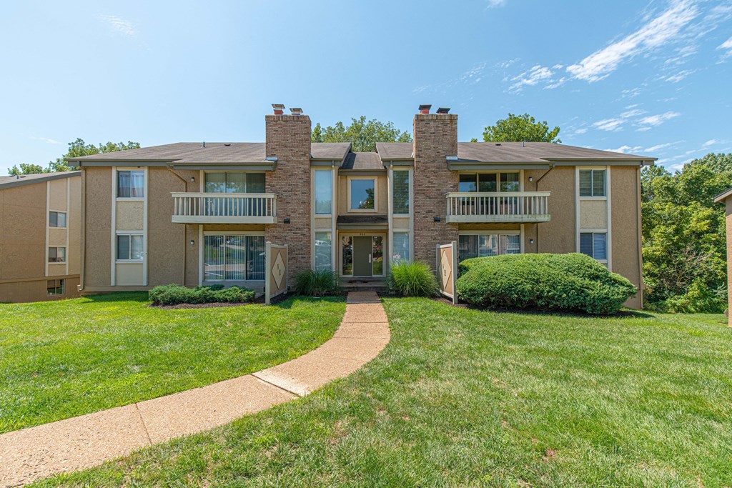 a walkway leading up to an apartment building with grass and bushes