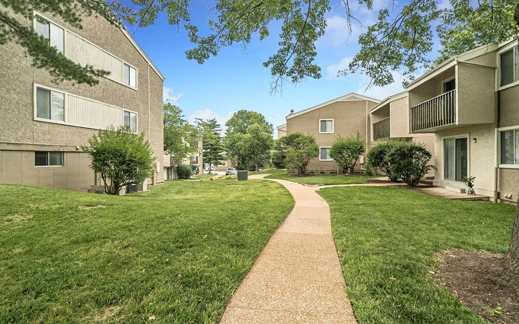 a walkway between two apartment buildings with grass and trees