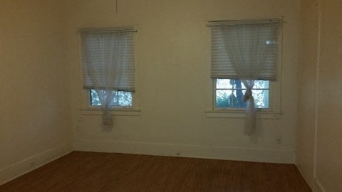 an empty room with two windows and a wooden floor