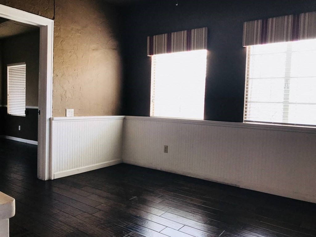 an empty room with dark wood floors and two windows