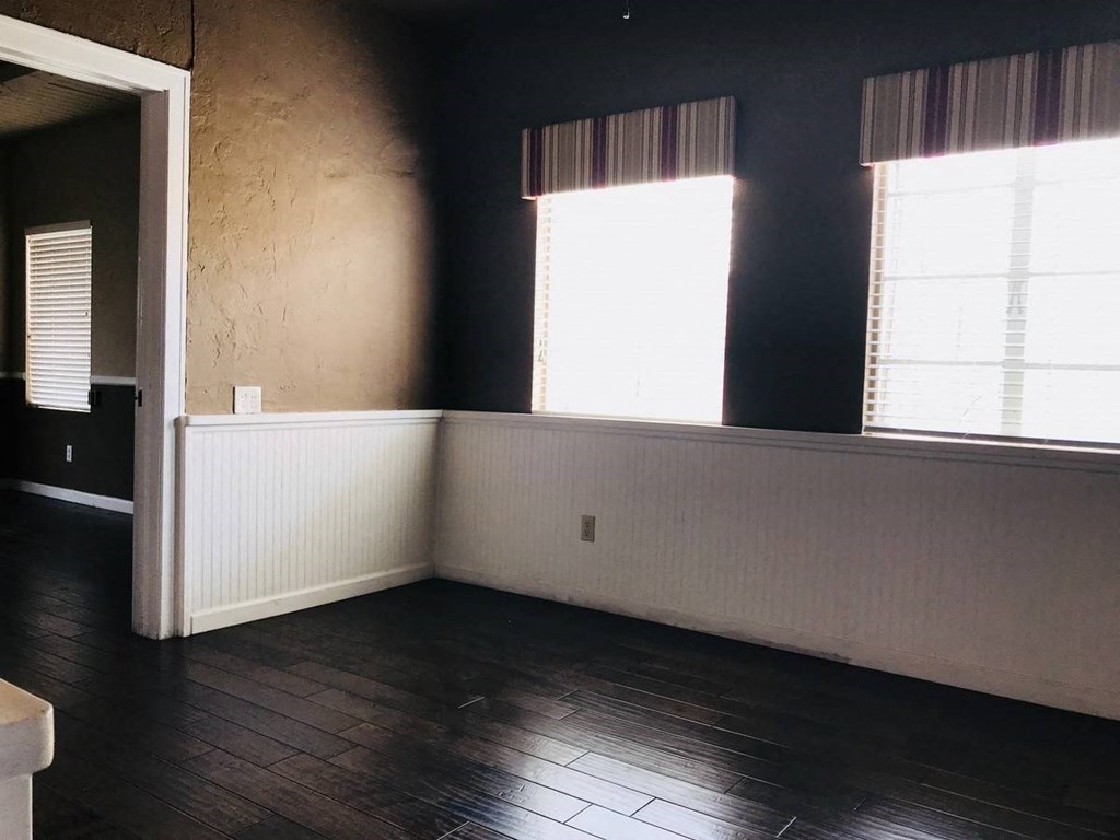 an empty room with dark wood floors and two windows