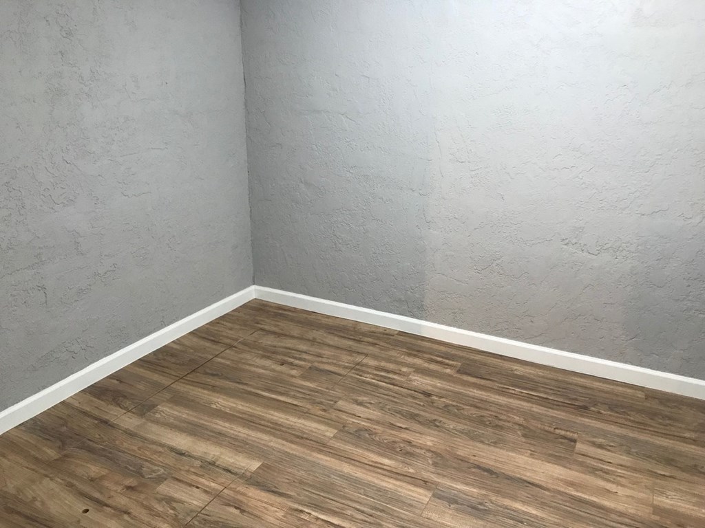 the corner of a room with wooden floors and a white wall