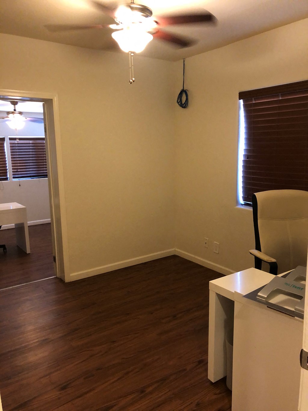 an empty living room with a desk and a ceiling fan