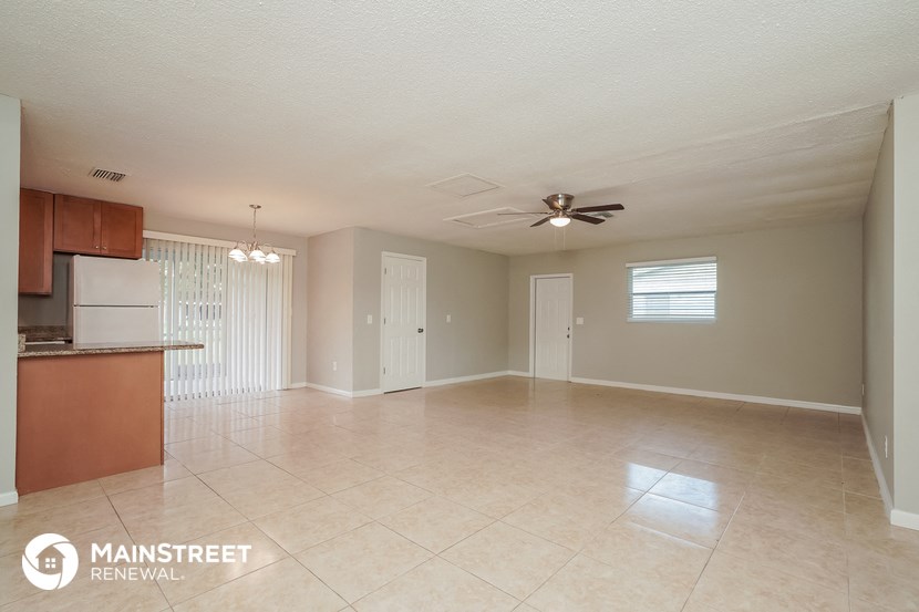 an empty living room with a kitchen and a ceiling fan