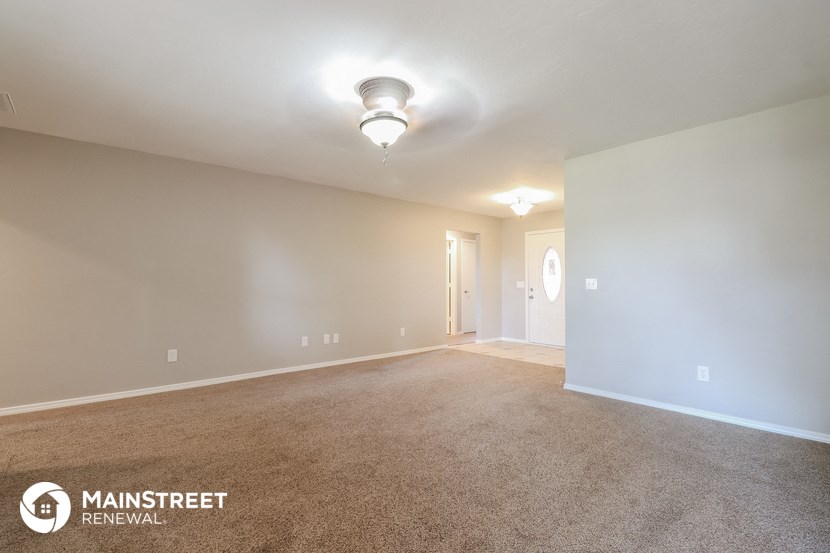 the spacious living room with carpeted flooring and white walls