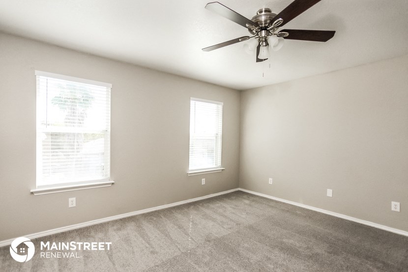 an empty room with a ceiling fan and two windows