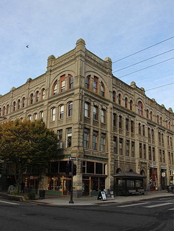 A large, old building with many windows sits on a street corner.