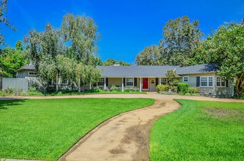 A house with a red door is surrounded by a green lawn and trees.