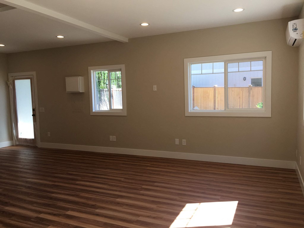 an empty living room with wooden floors and two windows