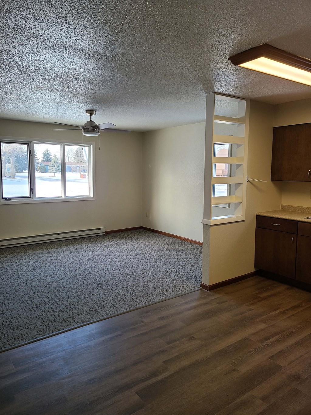 an empty living room with a kitchen and a window