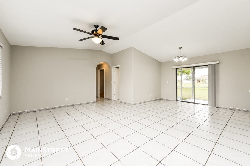 an empty living room with a ceiling fan and white tiles