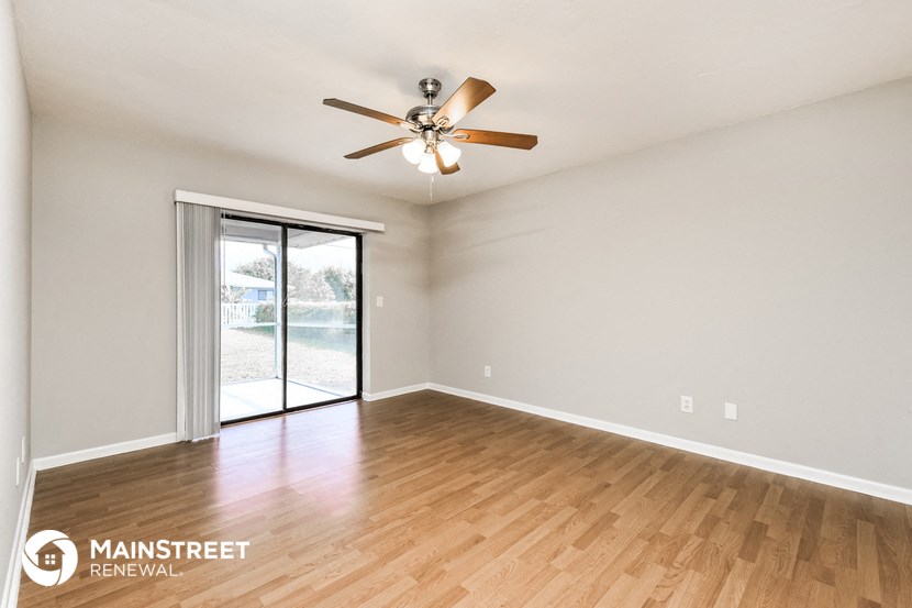 the spacious living room with wood flooring and a ceiling fan