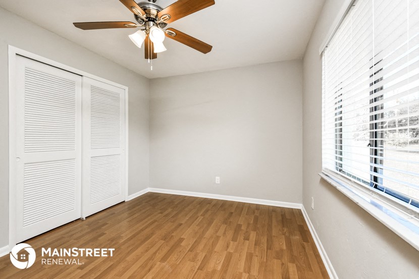 an empty living room with a ceiling fan and large windows