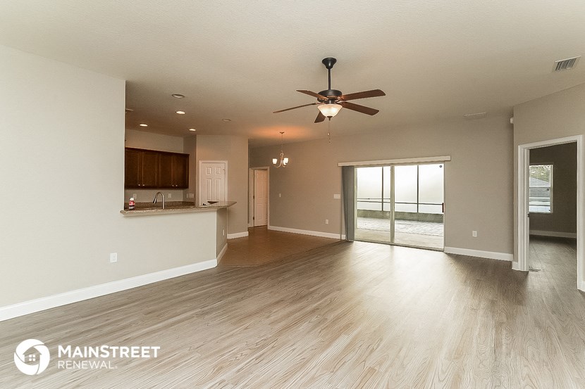 an empty living room with a ceiling fan and a kitchen