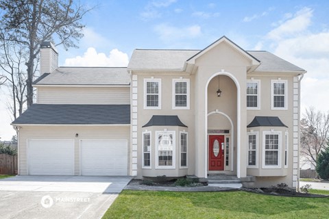 a beige house with a red door and a lawn