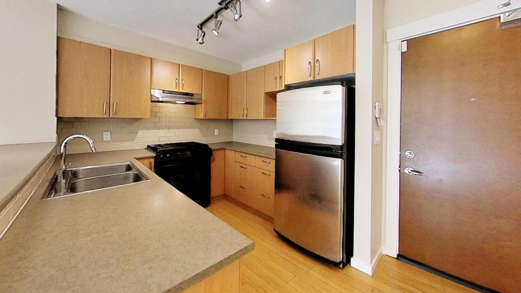 A kitchen with a refrigerator, sink, and cabinets.