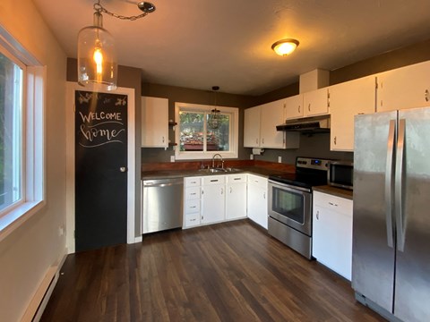 A kitchen with a black fridge and a chalkboard that says "Welcome Home".