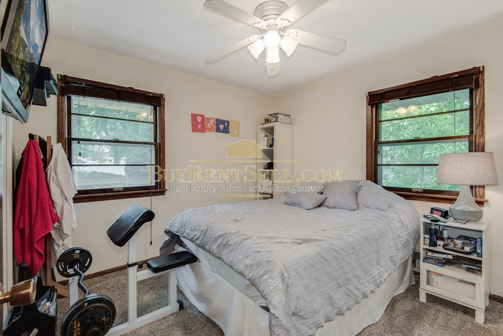 a bedroom with a bed and a fan and two windows
