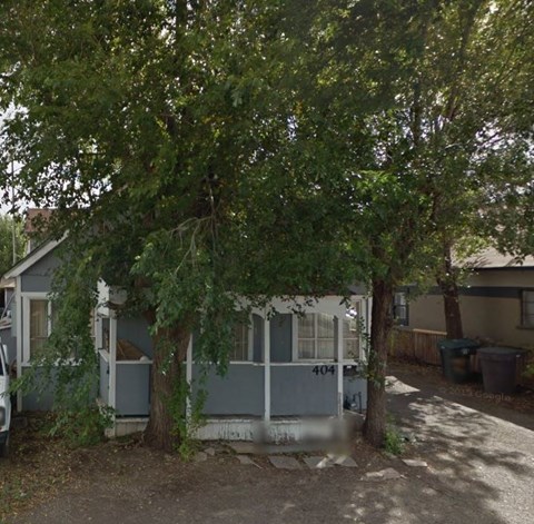 A tree with green leaves is in front of a grey house with the number 404 on it.