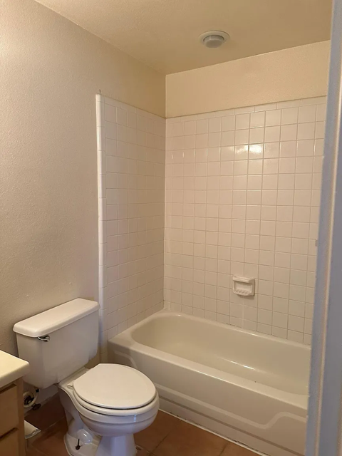 A white toilet and bathtub in a bathroom with white tiles.