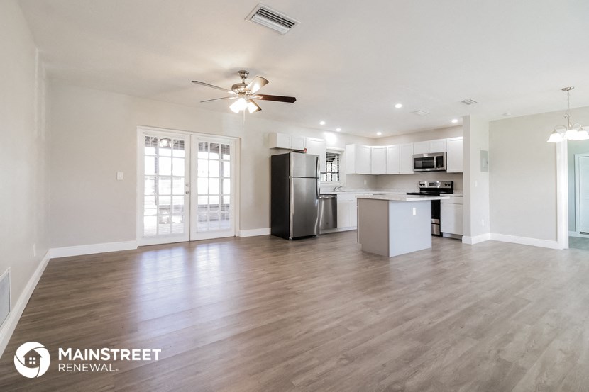 an empty living room with a kitchen and a ceiling fan