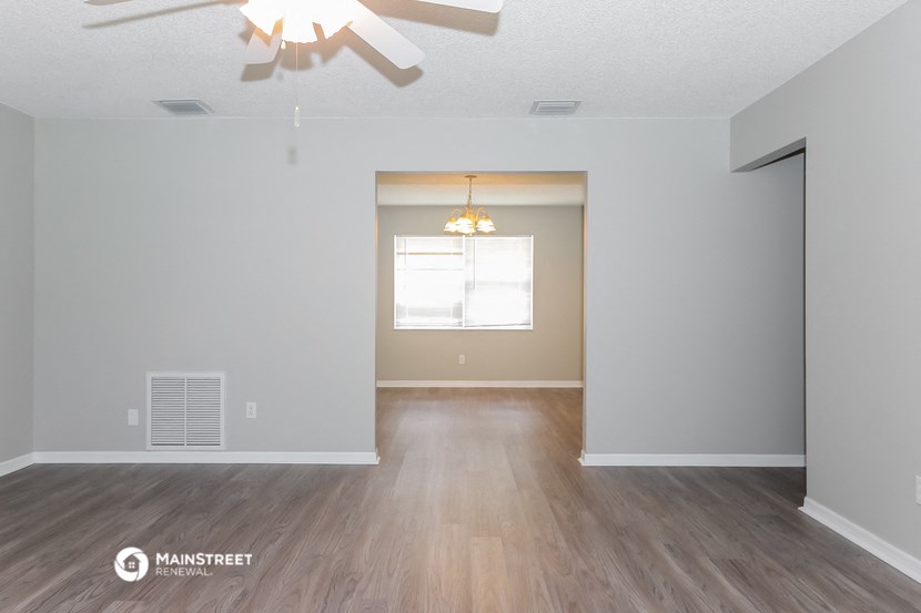 the spacious living room with hardwood flooring and a ceiling fan