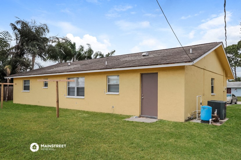 a small yellow house with a yard and a blue trash can